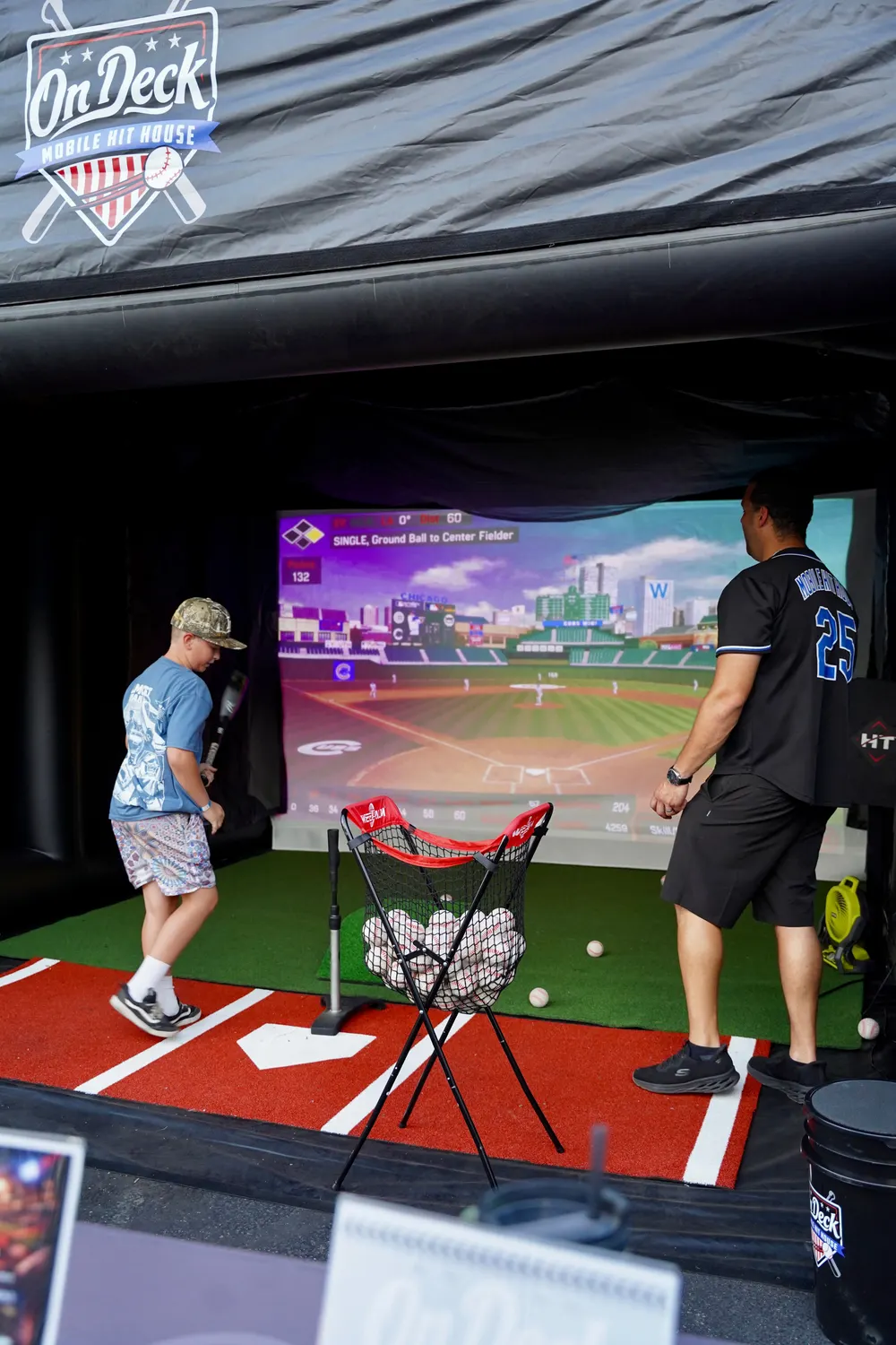 A young hitter and an On Deck coach inside the hit house, a big-league ballpark up on the HitTrax screen